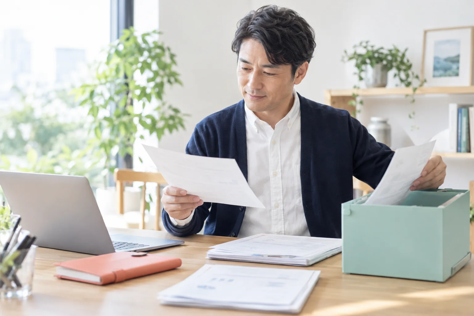 ノートPCと資料を見ながら残す原本と整理する資料を分ける架空の男性