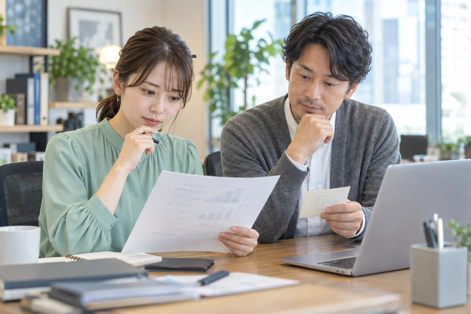 紙の資料とPCを比較し、再送依頼を相談する架空の二人